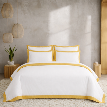 White bedding set with yellow trim on a bed in a room with wooden furniture and plants.