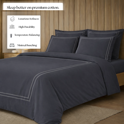 Dark gray bedding set on a bed with a wooden headboard, featuring text about premium cotton benefits.