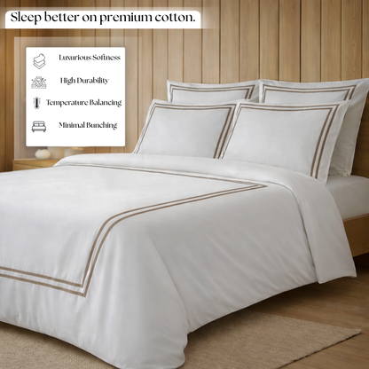 White bedding set with brown piping on a bed in a bedroom setting, featuring text about premium cotton benefits.