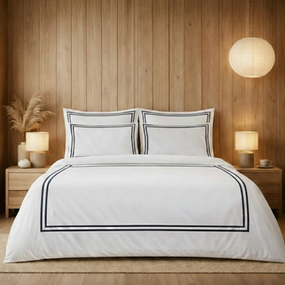 White bedding set with black trim on a bed in a bedroom with wooden walls and lamps.