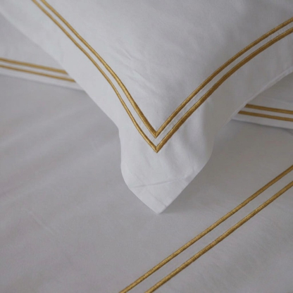 White pillow with gold trim on a matching white background